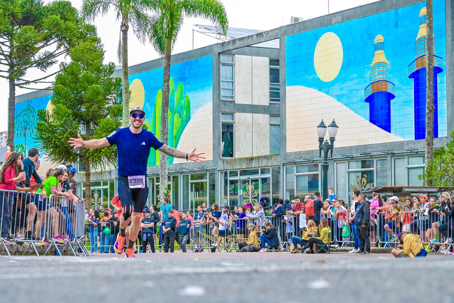 Corredor próximo à linha de chegada de uma maratona, com os braços abertos celebrando a conquista e curtindo a atmosfera