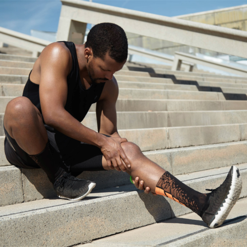 Atleta sentado segurando a perna com expressão de dor na região da canela